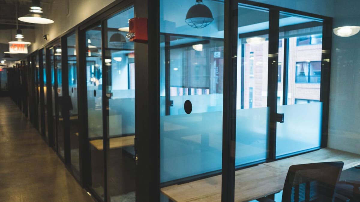 Cam bölmeli modern bir ofis koridorunda toplantı masası ve sandalyeler