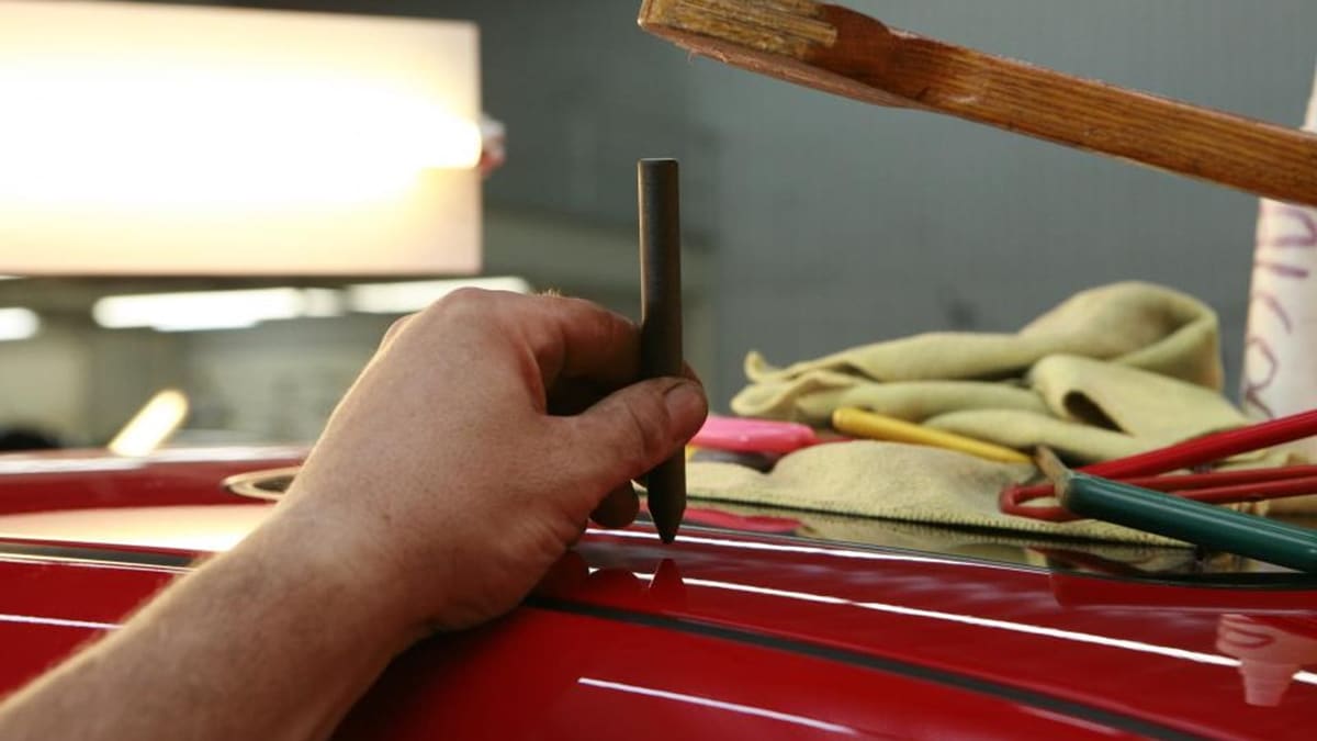 Kırmızı bir otomobilin kaportasındaki göçüğü özel bir el aletiyle düzelten usta