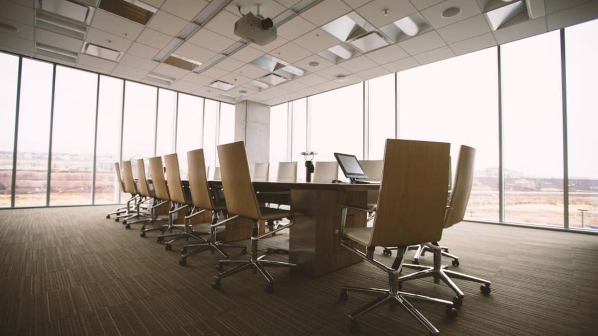 Cam cepheli bir ofis katında uzun toplantı masası ve çevresine dizilmiş yönetim koltukları
