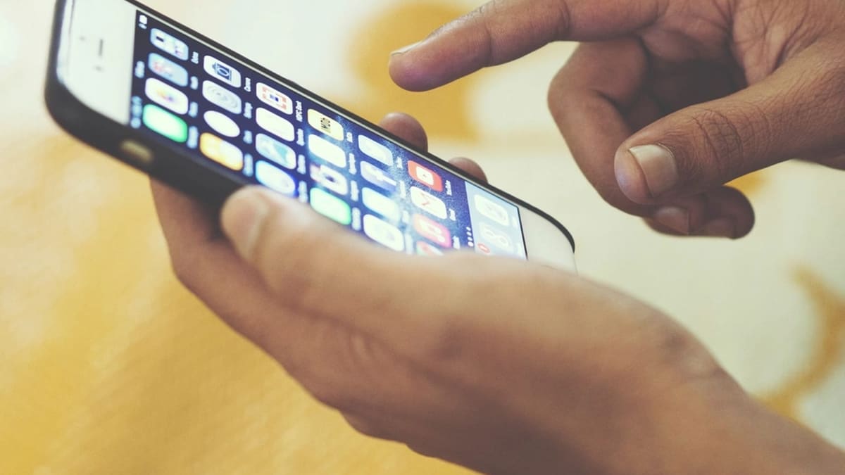 Elle tutulan akıllı telefon ekranında uygulama simgelerine dokunan parmaklar