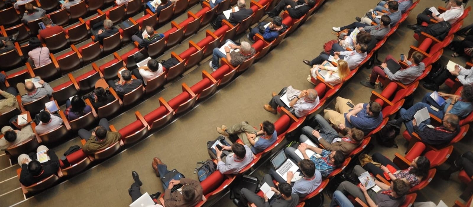 Kırmızı koltuklu konferans salonunda not alan katılımcıların yukarıdan görünümü