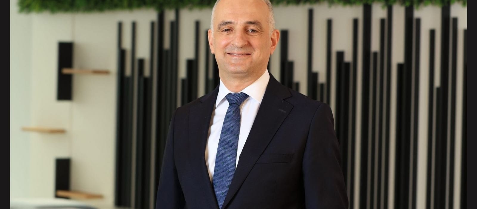 Yeşil bitki duvarı önünde çekilmiş bir Millî Reasürans yöneticisinin portresi