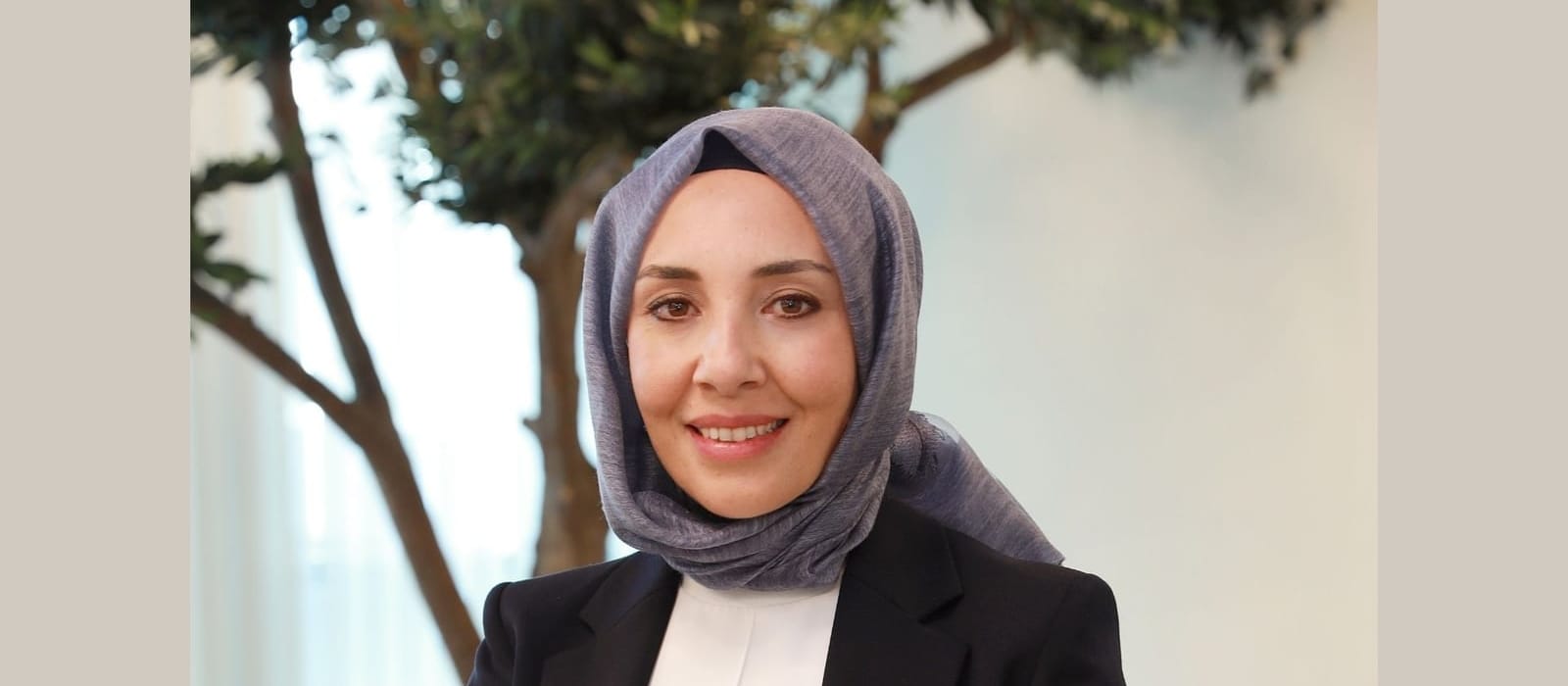 Bitkilerle çevrili ofiste çekilmiş başörtülü bir Neova Katılım Sigorta yöneticisinin portresi