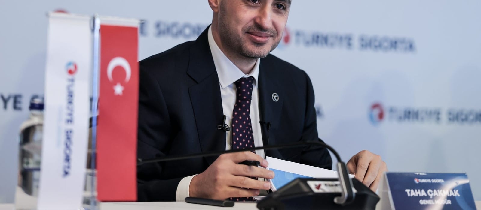 Türkiye Sigorta logolu fon önünde masada konuşan bir yönetici